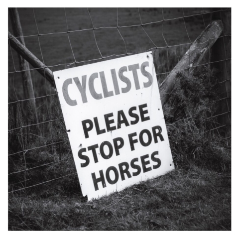 A sign saying 'CYCLISTS PLAESE STOP HERE FOR HORSES' is pinned to a wire fence on the footpath between Fairbourne and Morfa Mawddach