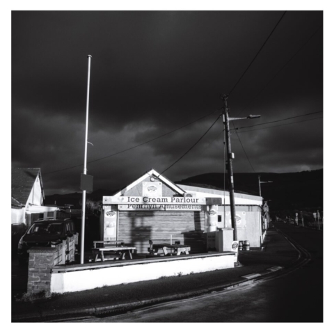 Single story 'Ice Cream Parlour' building wit picnic bench in the foreground and dark skies behind