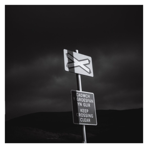 C'ADWCH GROESFAN IN GLIR - KEEP CROSSING CLEAR' sign with stormy skies in the background