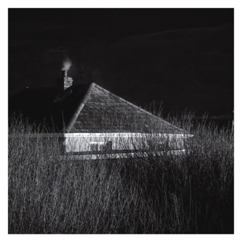 Bungalow roof with smoke rising from its chimney with grass land in front