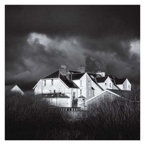 Row of large terrance houses with big exxtensions with grass land in front of them and dark skies behind them