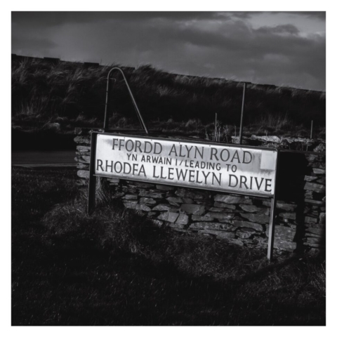'FFORDD ALYN ROAD - YN ARWAIN I / LEADING TO - RHODFA LLEWELLYN DRIVE' road name sign in front of a stone wall